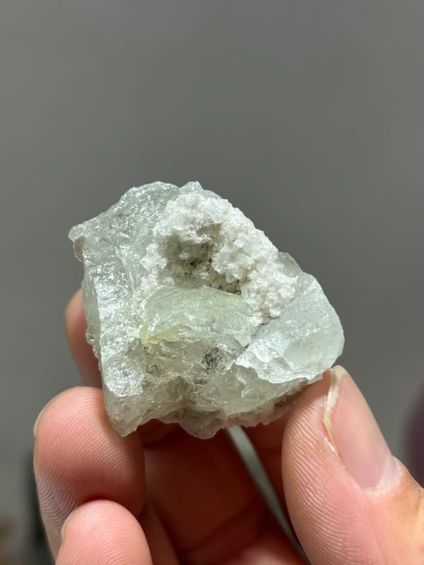 Pale aquamarine with white calcite in pocket from Xuebaoding, Sichuan, China, held in hand