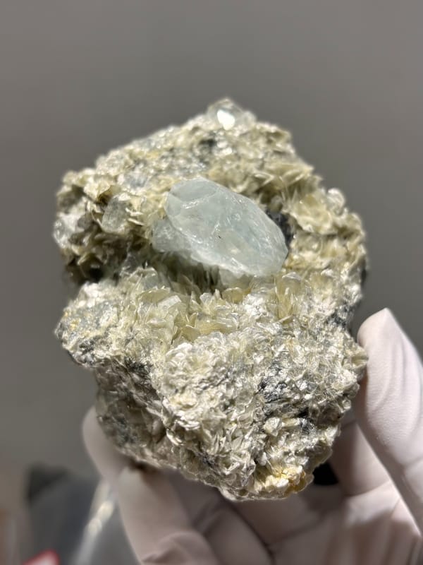 Pale aquamarine prism in tan mica with cassiterite from Xuebaoding, Sichuan, China, close-up of the crystal faces