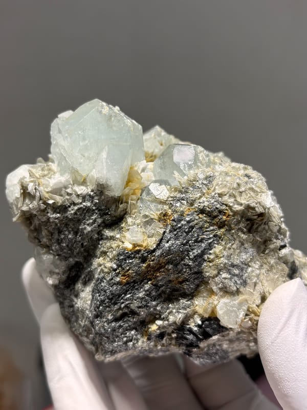 Pale aquamarine prism in tan mica with cassiterite from Xuebaoding, Sichuan, China, reverse side