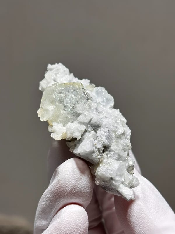 Pale aquamarine crystal on white feldspar from Xuebaoding, Sichuan, China, held in gloved hand