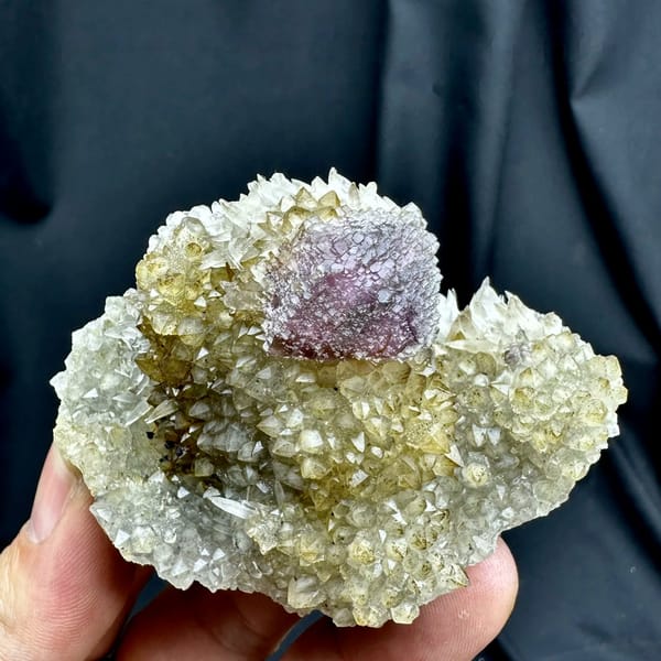 Purple-green fluorite octahedron on sparkling calcite matrix from Fujian, China, held in hand