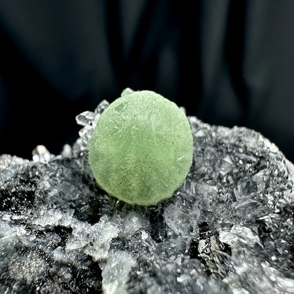 Green prehnite ball on black matrix with white quartz druse from Sichuan, China, close-up of the crystal faces
