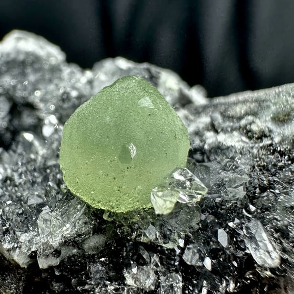 Green prehnite ball on black matrix with white quartz druse from Sichuan, China, top view