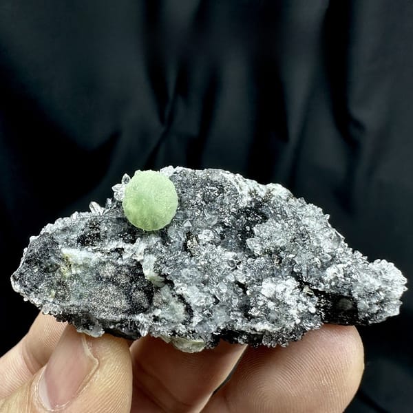 Green prehnite ball on black matrix with white quartz druse from Sichuan, China, detail of the matrix contact
