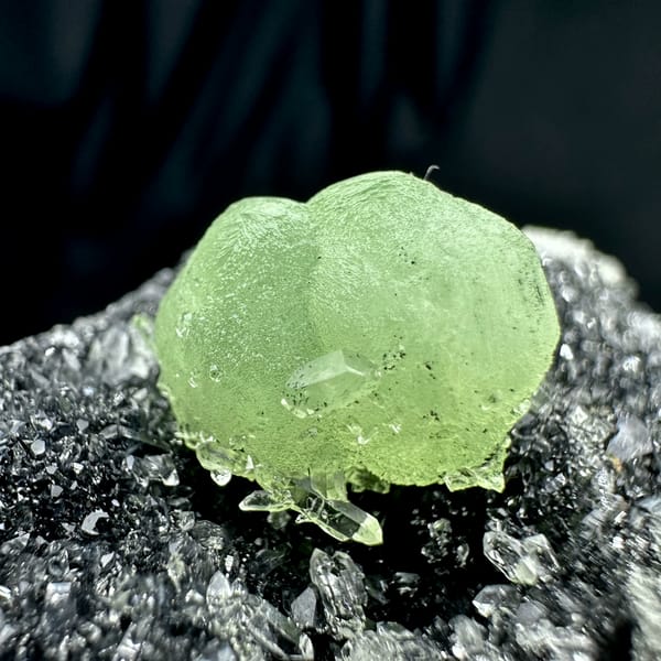 Apple-green prehnite sphere on dark matrix coated in quartz druse from Sichuan, China, close-up of the crystal faces