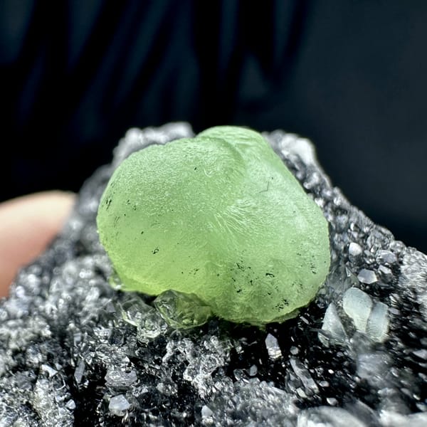 Apple-green prehnite sphere on dark matrix coated in quartz druse from Sichuan, China, top view