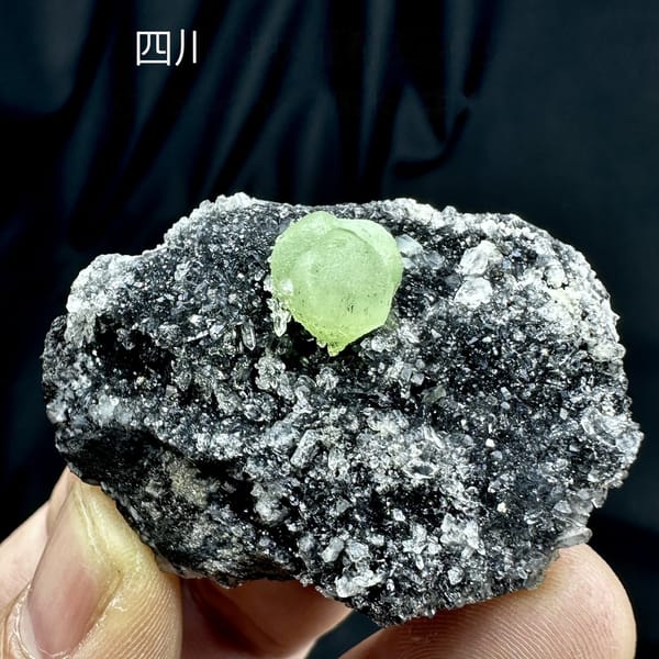 Apple-green prehnite sphere on dark matrix coated in quartz druse from Sichuan, China, detail of the matrix contact