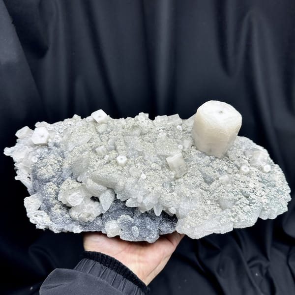 Large quartz druse plate with hexagonal calcite prism from Fujian, China, held in two hands, detail of the matrix contact