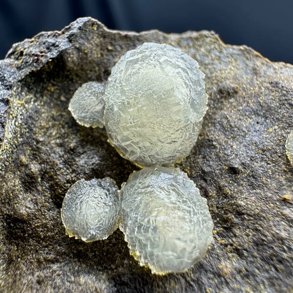 Cream-white botryoidal calcite balls on dark rock from Zhejiang, China, close-up of the crystal faces