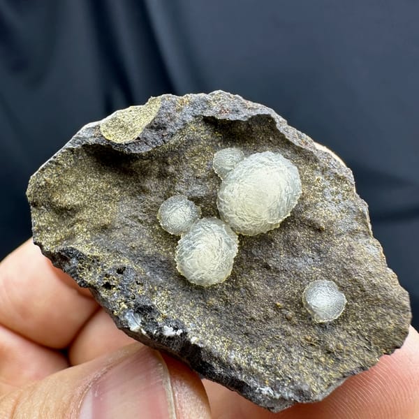 Cream-white botryoidal calcite balls on dark rock from Zhejiang, China, reverse side