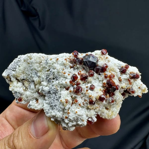 Wine-red garnet crystals with hyalite opal on feldspar from Yunxiao, Fujian, China, held in hand