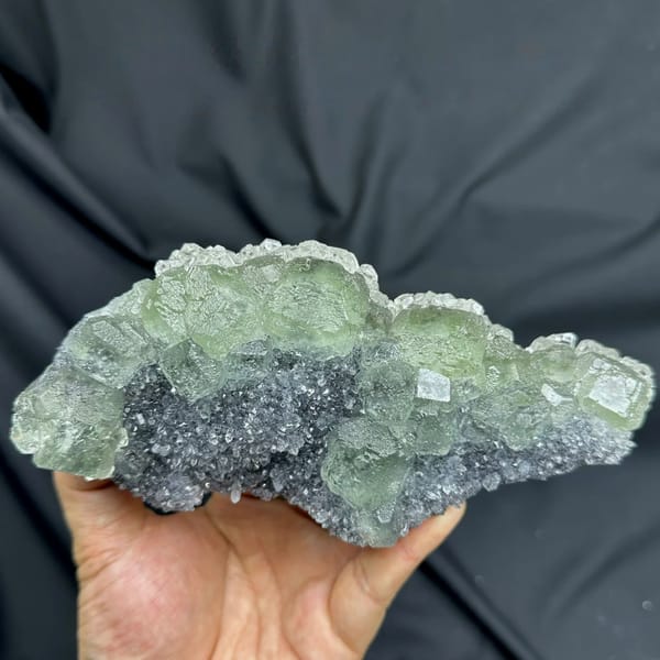 Long plate of pale green fluorite over grey quartz from Fujian, China, held in hand