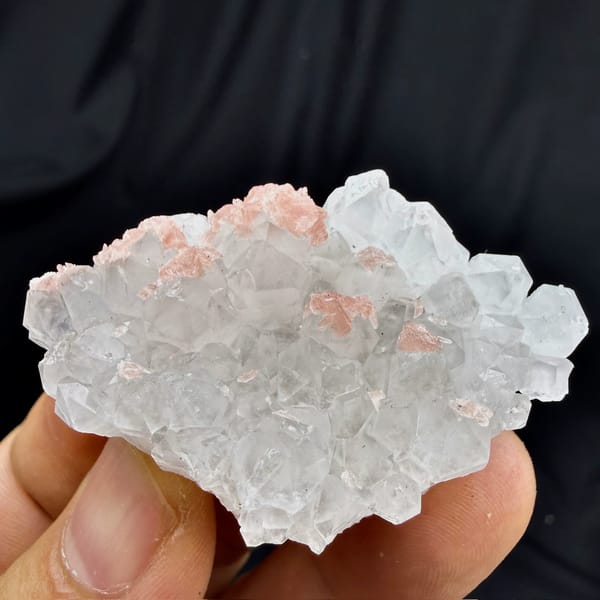 Pink rhodochrosite under frosted quartz crystals from Wuzhou, Guangxi, China, held in hand
