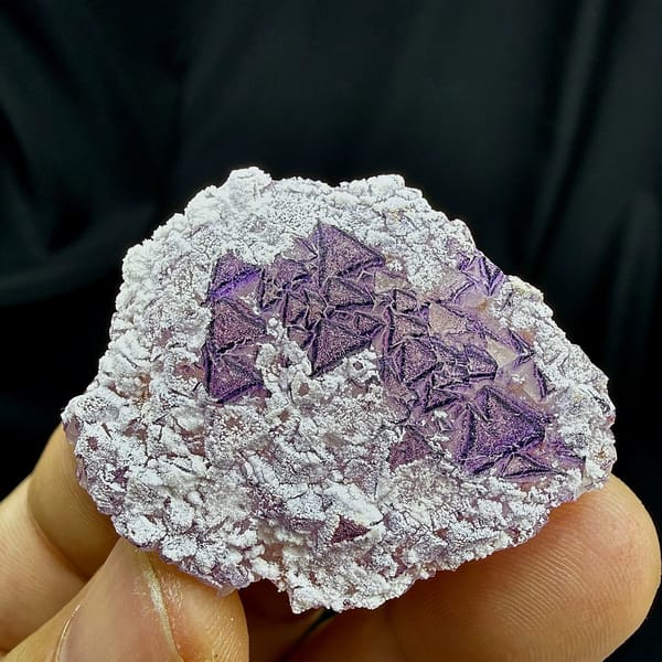 Deep purple triangular fluorite crystals in white aragonite from Yunnan, China, held in hand
