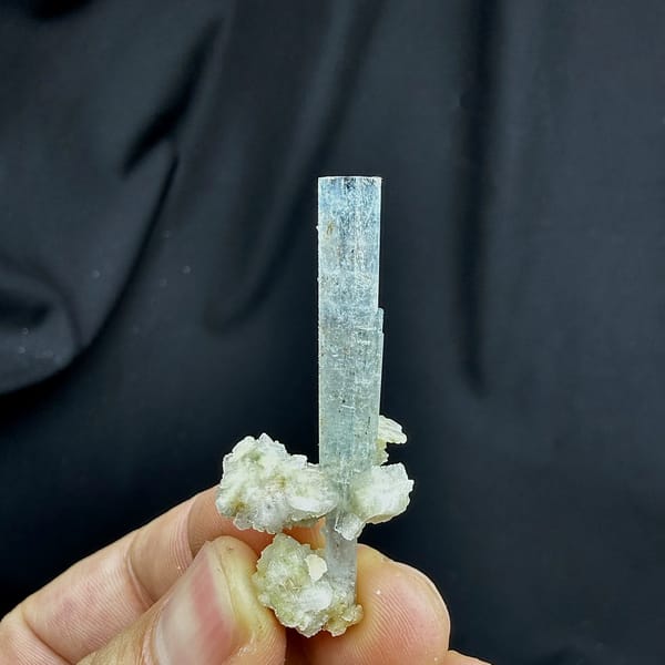 Sky-blue aquamarine prism standing on white feldspar from Namibia, held in hand
