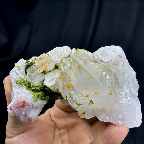 Milky garden quartz crystals with green epidote from Sichuan, China, held in hand