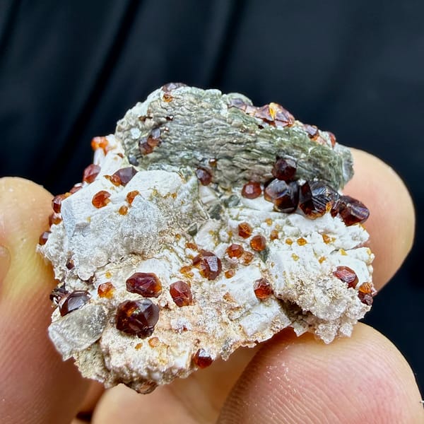 Dark-red garnets with mica and hyalite opal on feldspar from Yunxiao, Fujian, China, close-up of the crystal faces