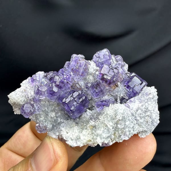 Violet-blue fluorite cubes on white quartz from Fujian, China, held in hand