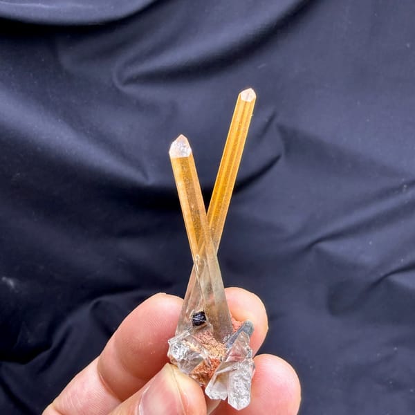 Two orange hematoid quartz needles on specular hematite from Guangdong, China, held in hand
