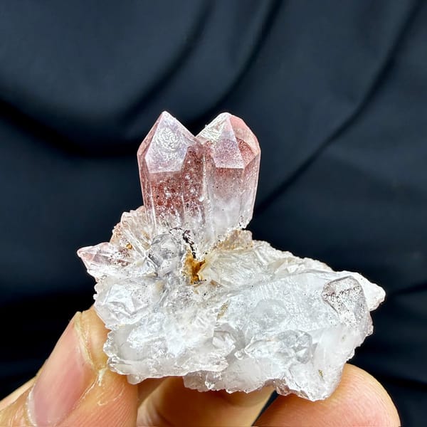 Strawberry-red phantom quartz crystal on white druse from Shanxi, China, held in hand