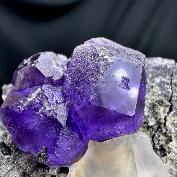 Etched violet-blue fluorite cubes with pale calcite on grey rock from Fujian, China, close-up of the crystal faces