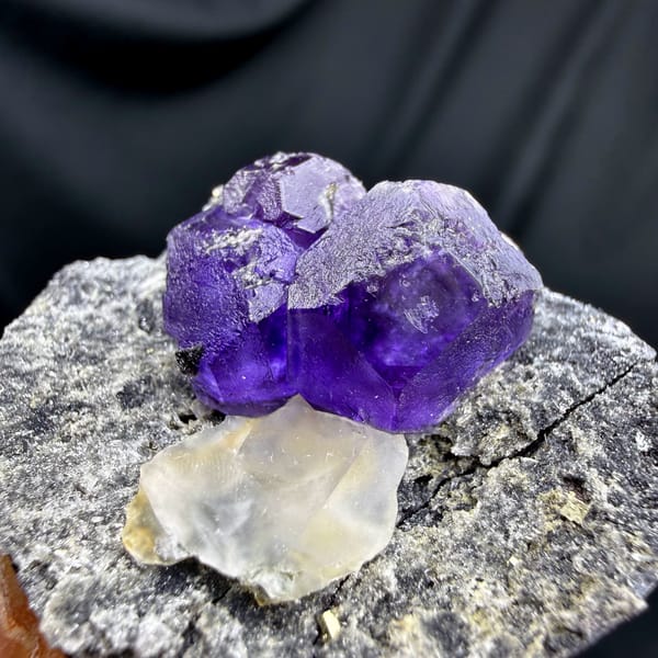 Etched violet-blue fluorite cubes with pale calcite on grey rock from Fujian, China, reverse side