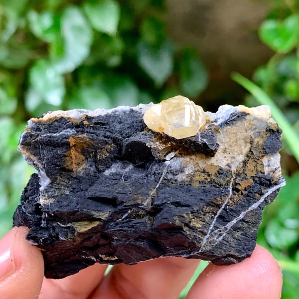 Pale yellow cerussite crystal on dark galena matrix from Guangxi, China, held in hand