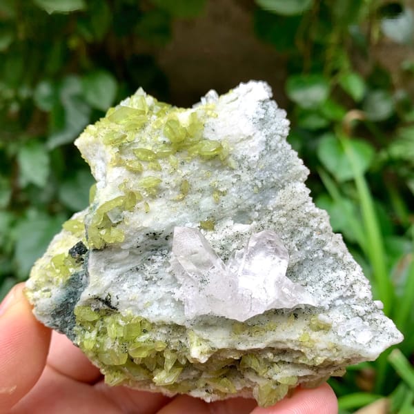 Clear quartz on green chlorite and feldspar with titanite from Pakistan, held in hand