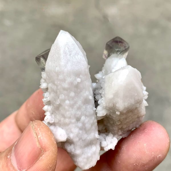 Pale quartz spire with small purple fluorite cubes from Inner Mongolia, China, held in hand