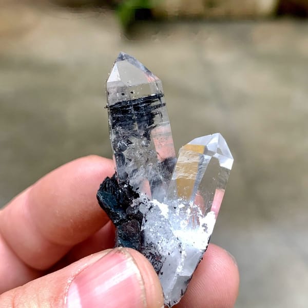 Two clear quartz prisms on black specular hematite from Guangdong, China, held in hand