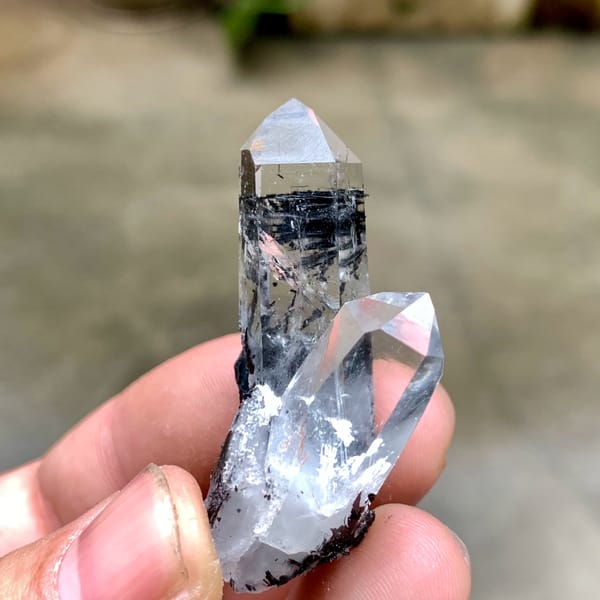 Two clear quartz prisms on black specular hematite from Guangdong, China, close-up of the crystal faces