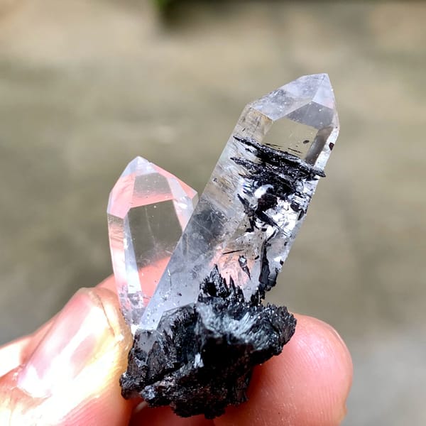 Two clear quartz prisms on black specular hematite from Guangdong, China, top view