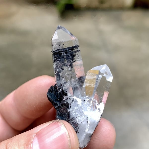 Two clear quartz prisms on black specular hematite from Guangdong, China, detail of the matrix contact
