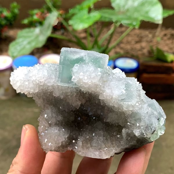 Bright green fluorite cube on sparkling quartz druse from Fujian, China, held in hand