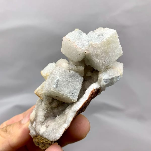 White sugar-frosted fluorite cubes on quartz from Fujian, China, held in hand
