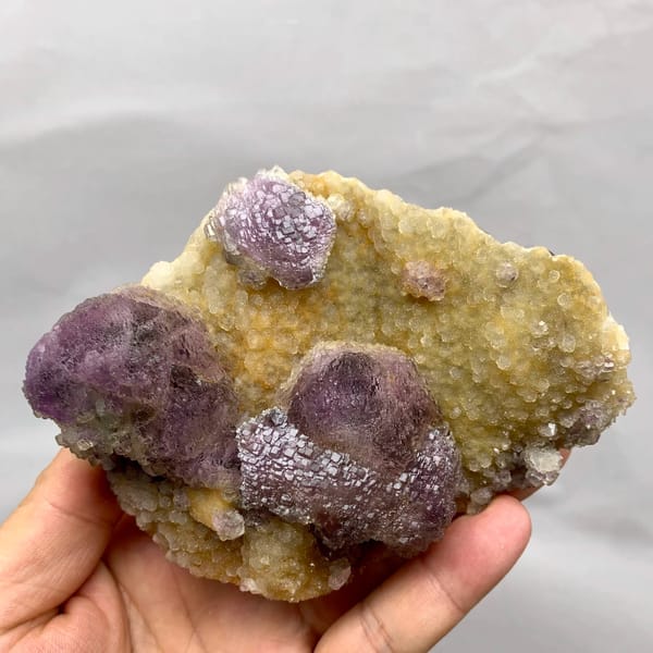 Purple mosaic fluorite balls on golden quartz druse from Fujian, China, held in hand