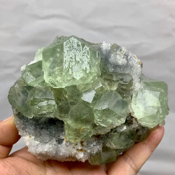 Cluster of large glassy sea-green fluorite cubes from Fujian, China, held in hand