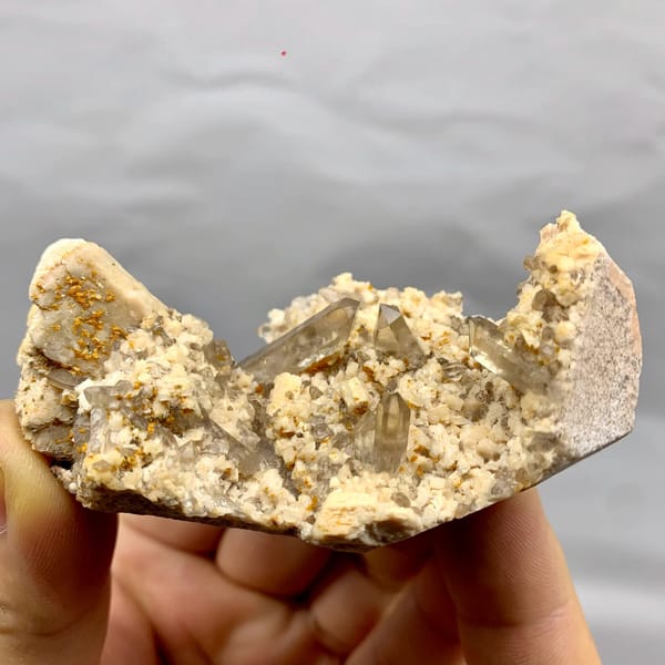 Smoky quartz points in hollow of cream feldspar from Fujian, China, held in hand