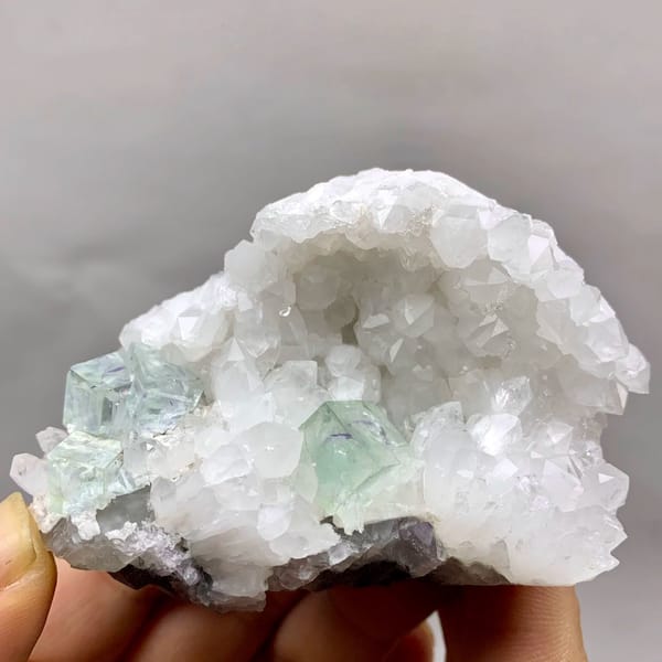 Glassy pale-green fluorite cubes in white quartz geode from Zhejiang, China, held in hand