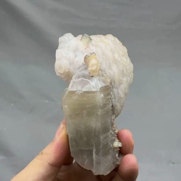 Pale quartz prism topped with layered white calcite from Inner Mongolia, China, held in hand