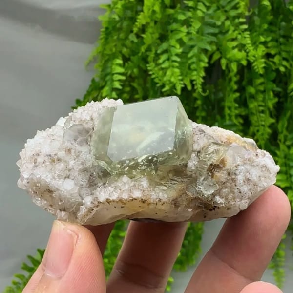 Glassy green fluorite dodecahedron on quartz druse from Fujian, China, held in hand