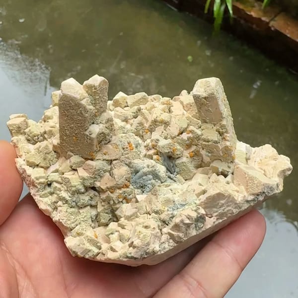 Tan feldspar towers with chabazite and bismuthinite from Yunxiao, Fujian, China, held in hand