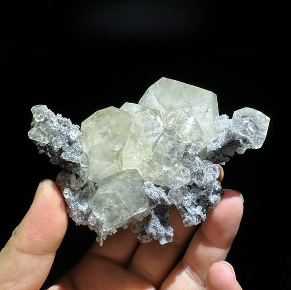 Glassy transparent calcite crystals on dark grey quartz from Fujian, China, held in hand