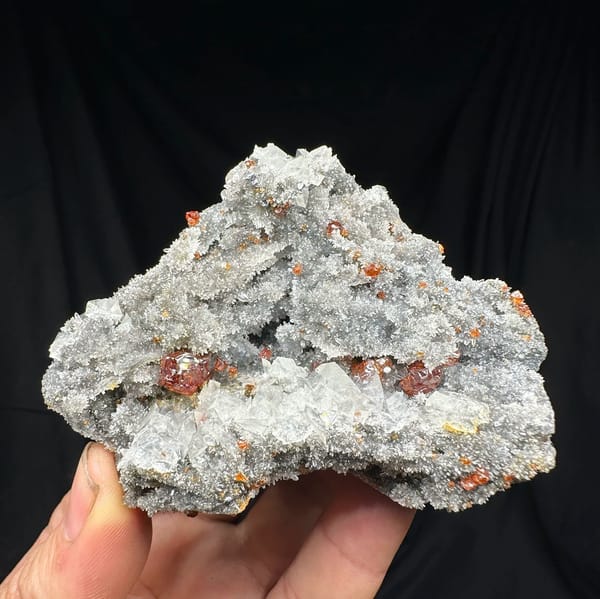 Red gem sphalerite crystals on grey calcite and quartz from Hunan, China, held in hand