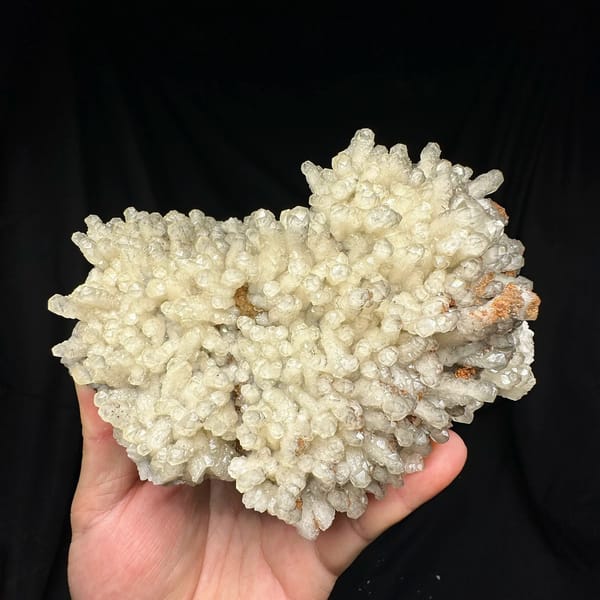 Plate of pale prismatic calcite crystals from Guizhou, China, held in hand
