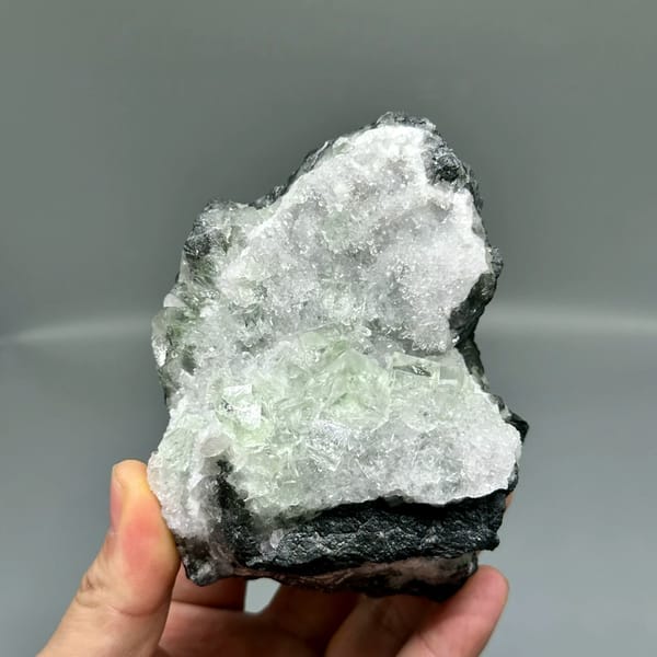 Glassy green fluorite under white quartz frosting from Zhejiang, China, held in hand