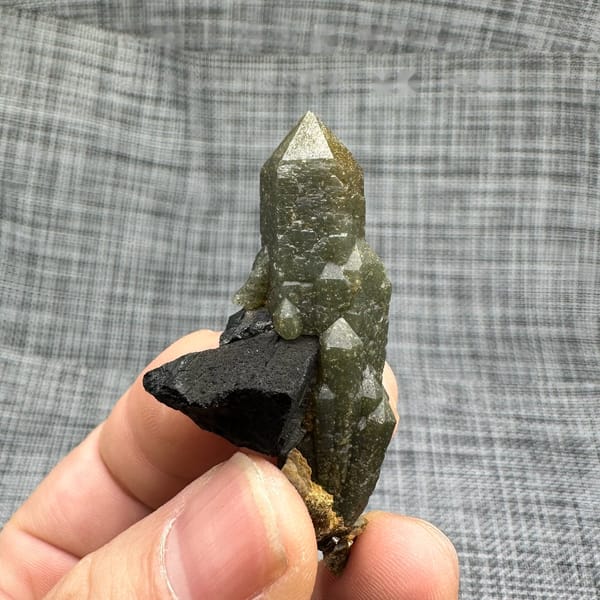 Green chlorite-coated quartz point on black matrix from Inner Mongolia, China, held in hand