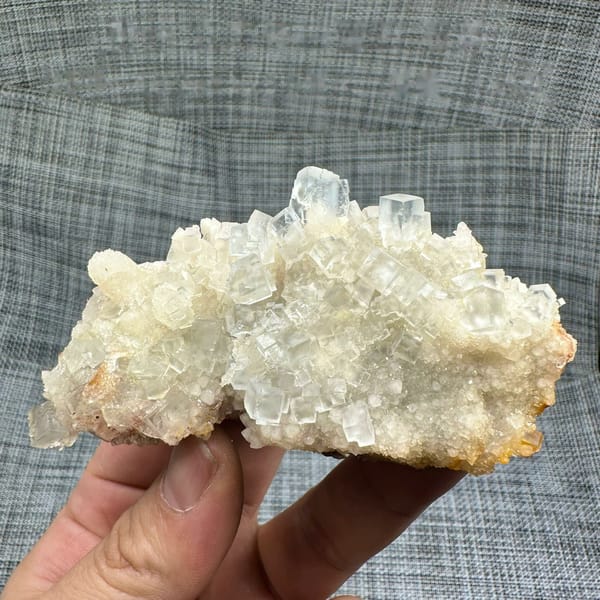 Colourless fluorite cubes on quartz plate from Guizhou, China, held in hand