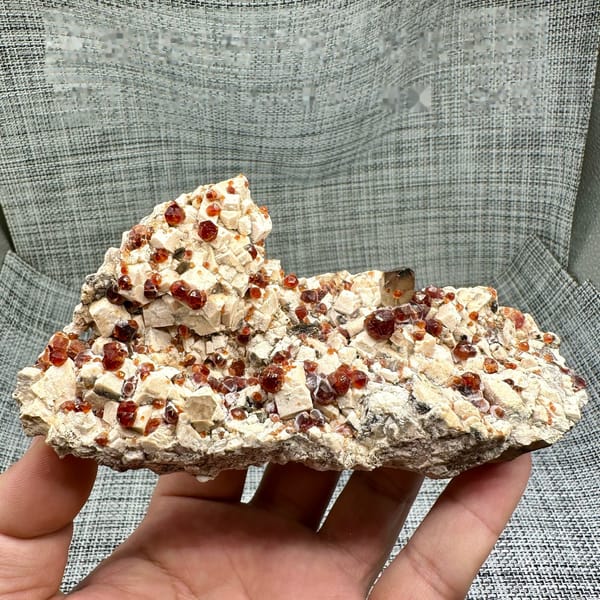 Feldspar plate peppered with wine-red garnets from Yunxiao, Fujian, China, held in hand
