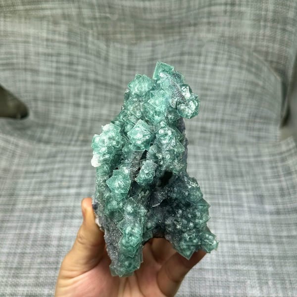 Teal-green octahedral fluorite with snowflake inclusions from Fujian, China, held in hand